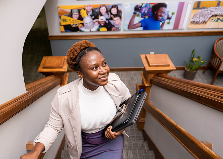 Student climbs the stairs in Main Hall with laptop in hand