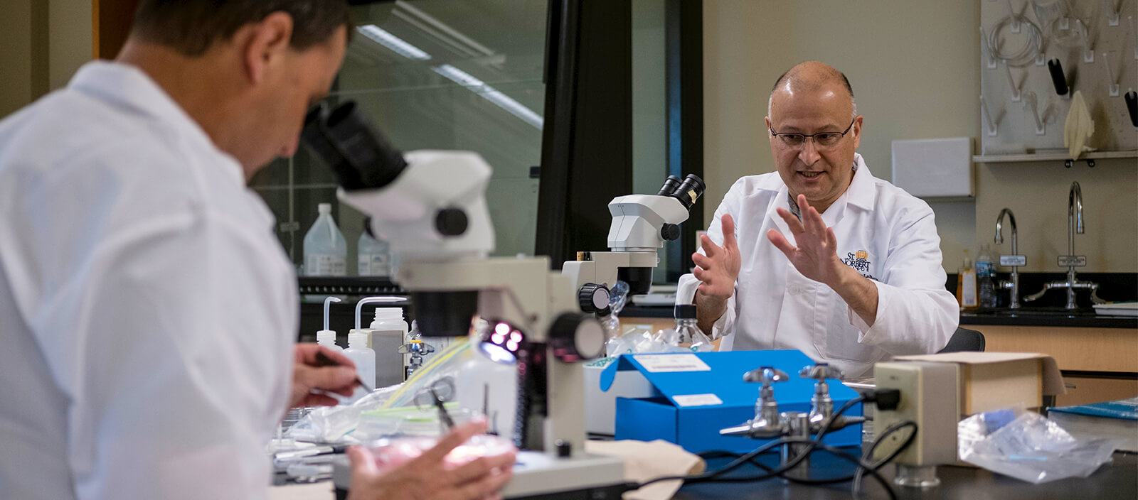 A professor works in front of a microscope in a science lab.